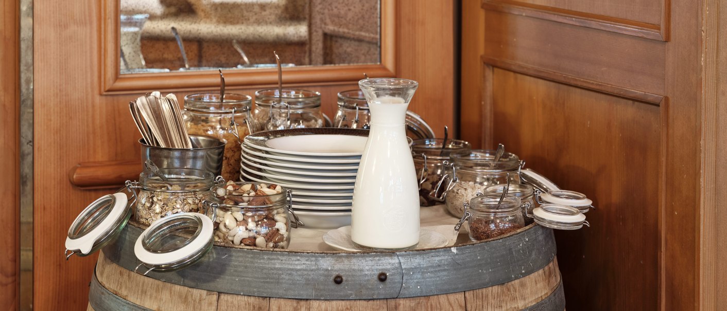 Ein Frühstücksbuffet auf einem Weinfass mit Milch, Nüssen, Besteck und Tellern in einem rustikalen Restaurant., © Badhotel Restaurant Stauferland