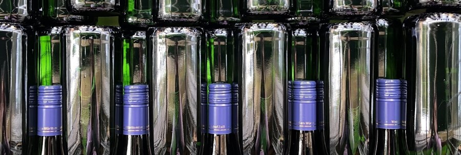 Stacked green wine bottles with blue caps on a shelf. The bottles reflect the light, creating a symmetrical pattern., © Weinhof Zaiß Stacked green wine bottles with blue caps on a shelf. The bottles reflect the light, creating a symmetrical pattern., © Weinhof Zaiß