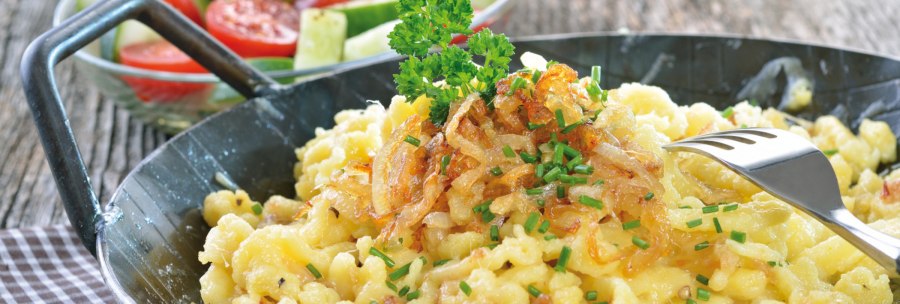 Käsespätzle mit Röstzwiebeln und Schnittlauch in einer Pfanne, daneben ein frischer Salat mit Tomaten und Gurken., © kab-vision - Fotolia