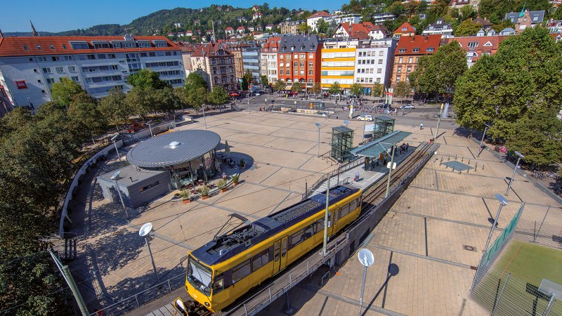 Aerial view of Marienplatz in Stuttgart. A yellow streetcar passes by, surrounded by trees and buildings. The square is lively and sunny., &copy; Stuttgart-Marketing GmbH