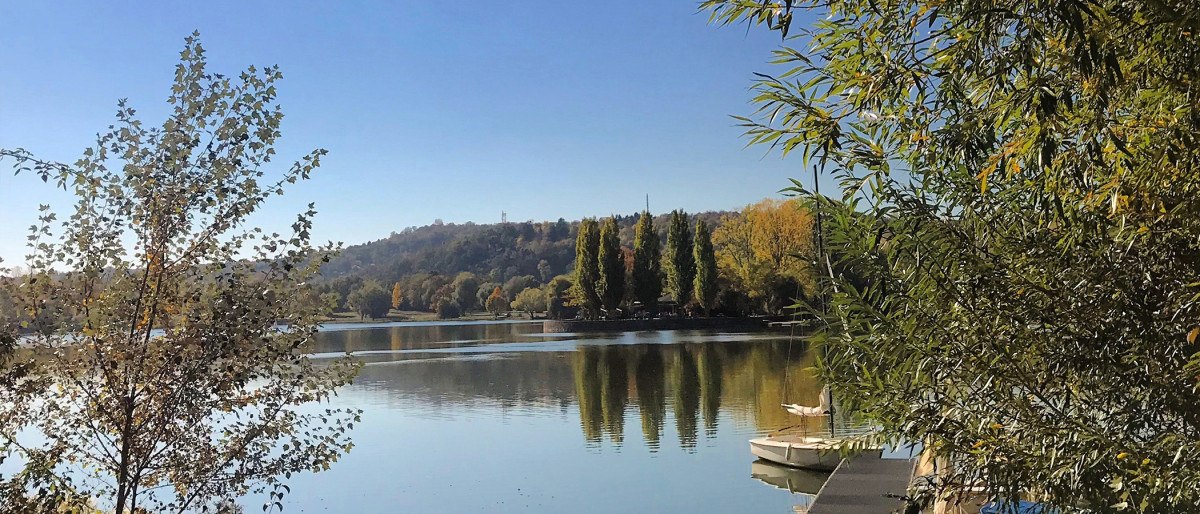 Lake Max-Eyth with calm water, surrounded by trees. A jetty and boats can be seen on the right-hand side of the picture., © Stuttgart-Marketing GmbH