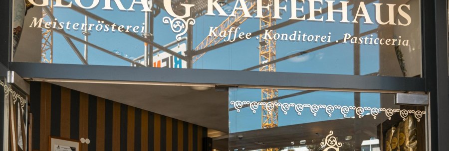 Entrance to the Glora coffee house with decorative lettering on the glass front. Construction cranes can be seen in the background., &copy; SMG, Sarah Schmid