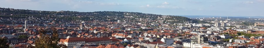 Panoramablick auf eine Stadt mit roten D&auml;chern, umgeben von gr&uuml;nen H&uuml;geln und blauem Himmel., &copy; SMG
