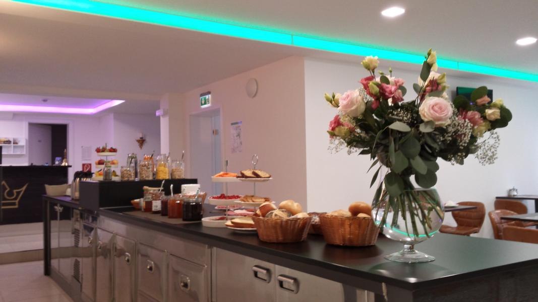 Frühstücksbüffet mit Brötchen, Aufschnitt und Marmeladen. Ein großer Blumenstrauß schmückt den Tisch. Im Hintergrund sind Sitzgelegenheiten zu sehen., © TOMAS