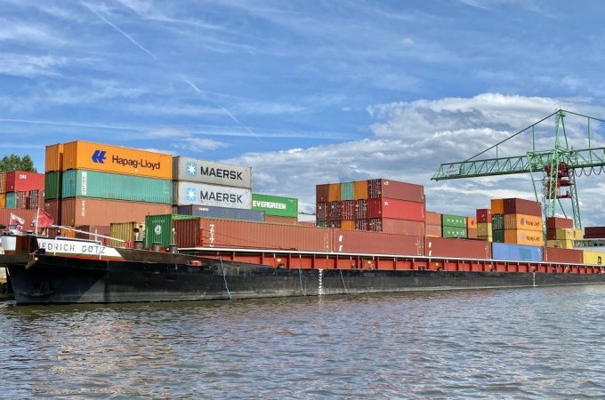 Ein Containerschiff im Stuttgarter Hafen mit bunten Containern und einem Kran im Hintergrund unter blauem Himmel., © Stuttgart Marketing GmbH Ein Containerschiff im Stuttgarter Hafen mit bunten Containern und einem Kran im Hintergrund unter blauem Himmel., © Stuttgart Marketing GmbH