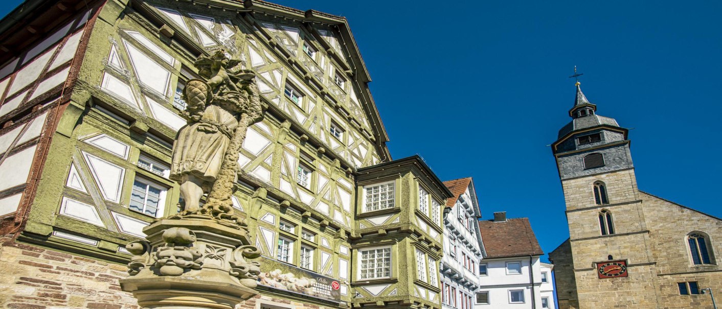 Statue in front of a half-timbered house and a church in Böblingen under a clear sky., © SMG Stuttgart Marketing GmbH - Sarah Schmid