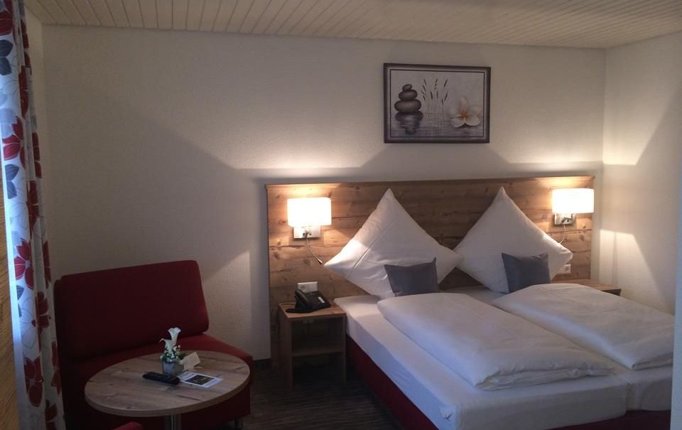 Cozy hotel room with double bed, red armchair, small wooden table and mural. Subtle lighting and bright walls create an inviting atmosphere., &copy; Hotel Lamm Hegnach