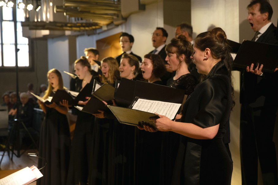 Ein Chor singt leidenschaftlich in einem Konzertsaal. Die S&auml;nger tragen schwarze Kleidung und halten Notenbl&auml;tter in der Hand., &copy; solistenensemble stimmkunst