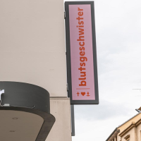 A store sign with the inscription 'blutsgeschwister' on a building. Another sign shows the logo with a heart and anchor., © Stuttgart-Marketing GmbH, Sarah Schmid A store sign with the inscription 'blutsgeschwister' on a building. Another sign shows the logo with a heart and anchor., © Stuttgart-Marketing GmbH, Sarah Schmid