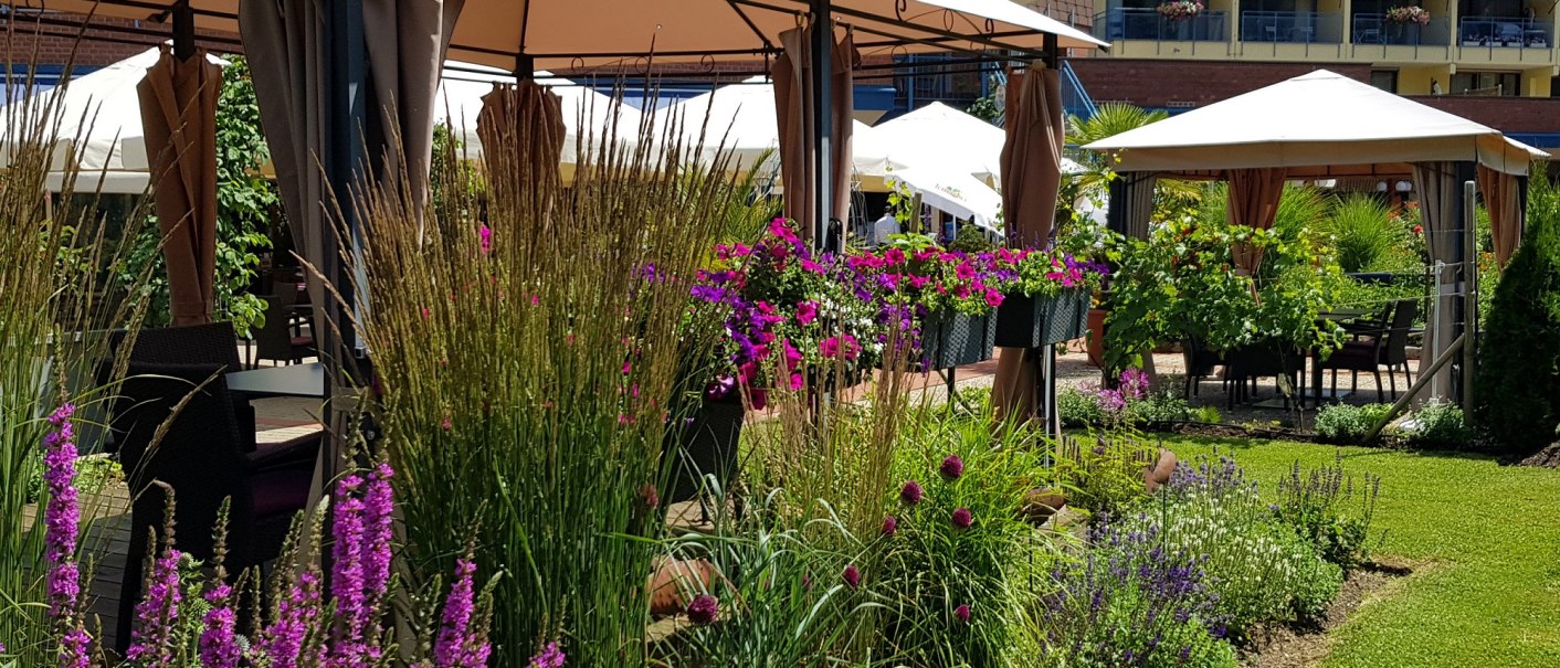 Garten mit Pavillons und blühenden Pflanzen vor dem Hotel Graf Eberhard. Im Hintergrund ist das Hotelgebäude zu sehen., © ©hotel-graf-eberhard.de