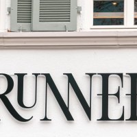 Schriftzug an der Hausfassade des Brunner Restaurants mit Serifen. Dar&uuml;ber Sprossenfenster mit gr&uuml;nen Fensterl&auml;den., &copy; SMG, Sarah Schmid