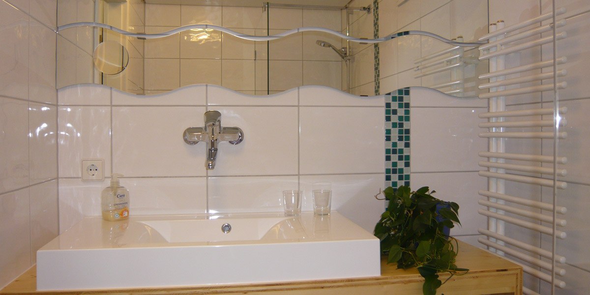 Modern bathroom with white washbasin, wave-shaped mirror, towel radiator and green plant., &copy; Hotel Hochwald