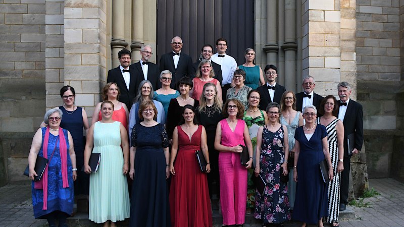 Der Motettenchor Stuttgart posiert in eleganter Kleidung vor einem historischen Gebäude., © Motettenchor Stuttgart Der Motettenchor Stuttgart posiert in eleganter Kleidung vor einem historischen Gebäude., © Motettenchor Stuttgart