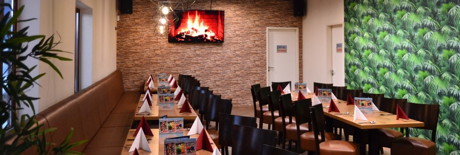 Ein langer Tisch in einer Lounge, dekoriert mit roten und weißen Servietten. An der Wand ein Bildschirm mit Kaminfeuer, daneben eine grüne Tapete., © Bowling & Billard Lounge Ein langer Tisch in einer Lounge, dekoriert mit roten und weißen Servietten. An der Wand ein Bildschirm mit Kaminfeuer, daneben eine grüne Tapete., © Bowling & Billard Lounge
