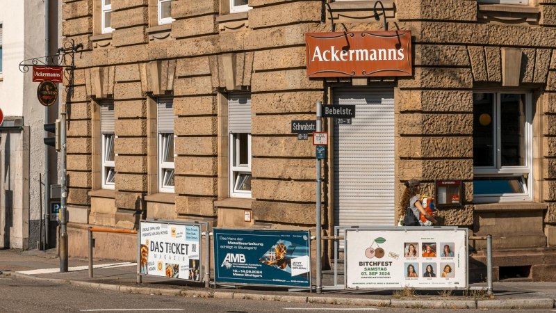 Eckgebäude mit dem Schild 'Ackermanns' an der Fassade. Straßenschilder für Bebelstr. und Schwabstr. sind sichtbar, ebenso mehrere Werbeplakate., © SMG, Sarah Schmid