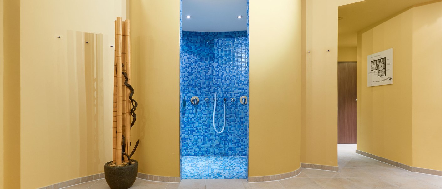 Ein Spa-Bereich mit einer blauen Mosaikdusche in der Mitte, umgeben von gelben Wänden und dekorativen Bambusstäben., © TOMAS Ein Spa-Bereich mit einer blauen Mosaikdusche in der Mitte, umgeben von gelben Wänden und dekorativen Bambusstäben., © TOMAS