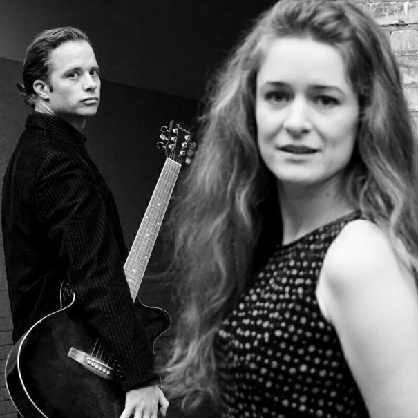 A man with a guitar looks seriously into the camera, while a woman in the foreground smiles slightly. Black and white photography with an artistic flair., &copy; Theaterhaus Stuttgart e.V.