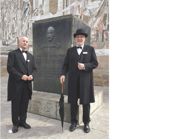Zwei M&auml;nner in historischer Kleidung posieren vor einem Gottlieb-Daimler-Denkmal in Schorndorf. Sie tragen Anz&uuml;ge und H&uuml;te und halten Regenschirme., &copy; Eigenbetrieb Tourismus und Citymanagement Schorndorf