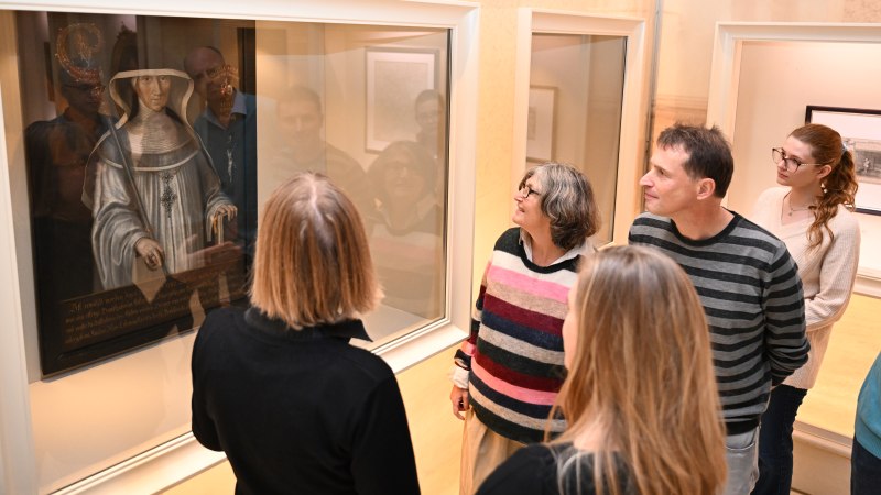 Eine Gruppe von Menschen betrachtet ein Gemälde in einem Museum. Sie stehen vor einer Vitrine und diskutieren interessiert., © HdGBW/ Franziska Kraufmann Eine Gruppe von Menschen betrachtet ein Gemälde in einem Museum. Sie stehen vor einer Vitrine und diskutieren interessiert., © HdGBW/ Franziska Kraufmann