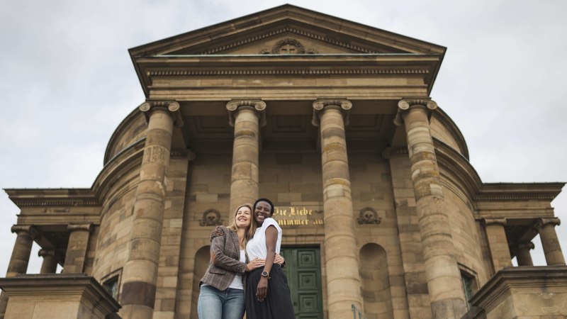 Two people embrace with a smile in front of the imposing façade of the Stuttgart burial chapel with its columns., © Stuttgart-Marketing GmbH, wpsteinheisser