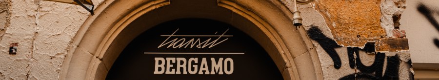 Steinrelief eines Kindes &uuml;ber einem Eingang mit der Aufschrift 'transit Bergamo'. Der Putz ist br&ouml;ckelig, Graffiti und Markisen sind sichtbar., &copy; SMG_Sarah Schmid