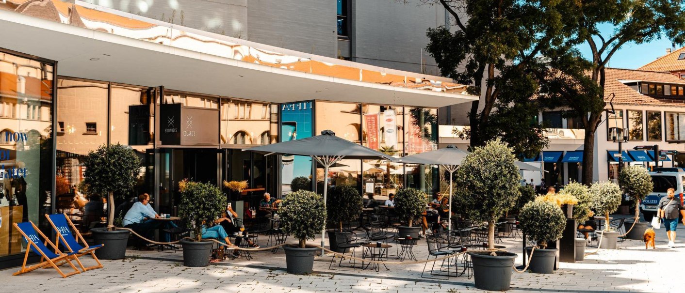 Außenbereich eines Cafés mit Tischen, Stühlen und Sonnenschirmen. Menschen sitzen und entspannen. Pflanzen in Töpfen dekorieren den Bereich., © Stuttgart Marketing GmbH, Sarah Schmid Außenbereich eines Cafés mit Tischen, Stühlen und Sonnenschirmen. Menschen sitzen und entspannen. Pflanzen in Töpfen dekorieren den Bereich., © Stuttgart Marketing GmbH, Sarah Schmid