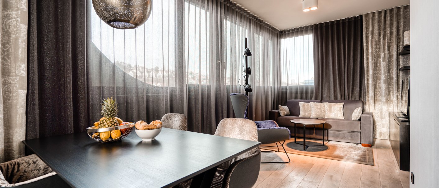 Moderne Suite mit stilvollem Esstisch, Obstschale, gemütlichem Sofa und großen Fenstern mit eleganten Vorhängen., © CLOUD N°7 APARTMENTS GmbH Moderne Suite mit stilvollem Esstisch, Obstschale, gemütlichem Sofa und großen Fenstern mit eleganten Vorhängen., © CLOUD N°7 APARTMENTS GmbH