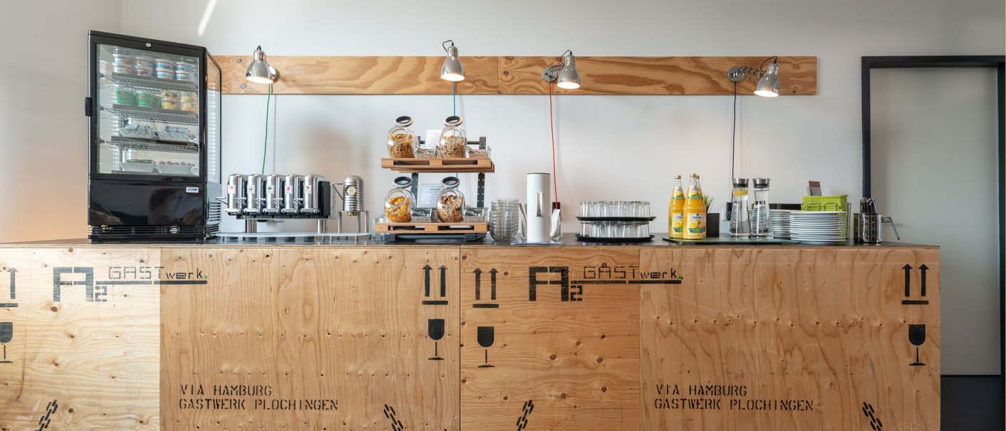 A modern breakfast area with a counter made of wooden pallets, drinks, snacks and a coffee machine. Bright, minimalist furnishings., &copy; a2 HOTELS Plochingen