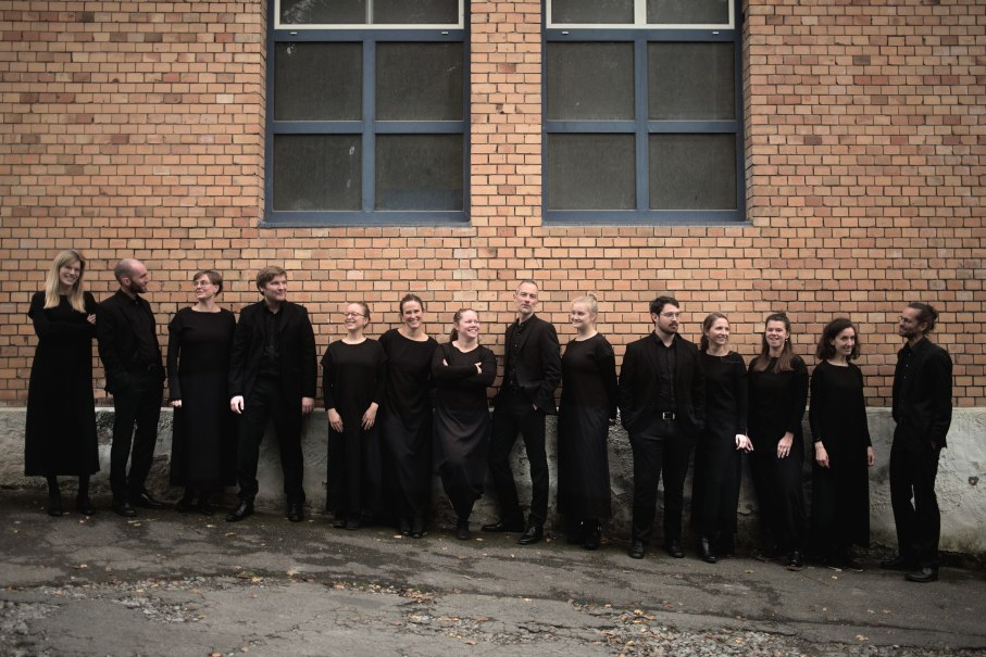 Eine Gruppe von 14 Personen in schwarzer Kleidung steht lächelnd vor einer Backsteinmauer mit Fenstern., © Kammerchor Vokalkunst / Daniel Radde Eine Gruppe von 14 Personen in schwarzer Kleidung steht lächelnd vor einer Backsteinmauer mit Fenstern., © Kammerchor Vokalkunst / Daniel Radde