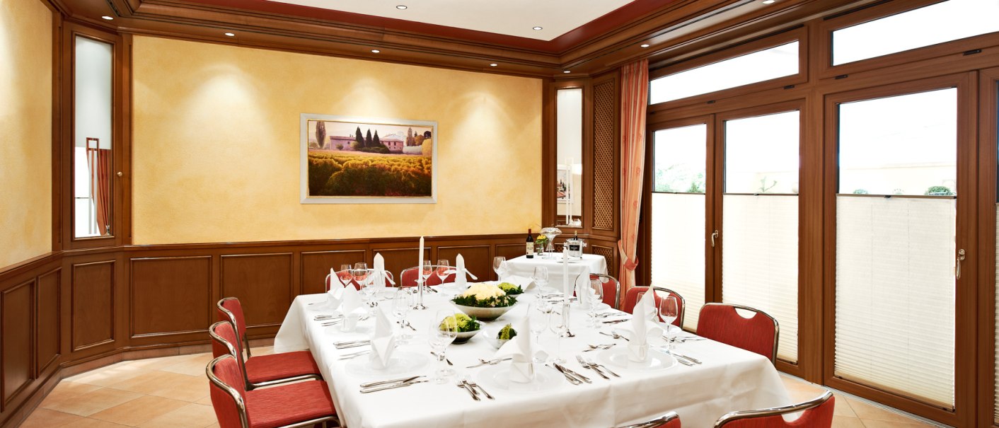 Elegantes Bankettzimmer mit gedecktem Tisch, roten Stühlen und großen Fenstern. An der Wand hängt ein Landschaftsbild., © Hirsch Hotel