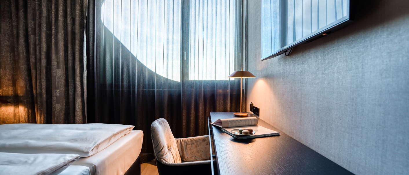 Modernes Hotelzimmer mit elegantem Schreibtisch, gemütlichem Stuhl, Doppelbett und großem Fenster mit Vorhängen. Ein Fernseher hängt an der Wand., © CLOUD N°7 APARTMENTS GmbH Modernes Hotelzimmer mit elegantem Schreibtisch, gemütlichem Stuhl, Doppelbett und großem Fenster mit Vorhängen. Ein Fernseher hängt an der Wand., © CLOUD N°7 APARTMENTS GmbH
