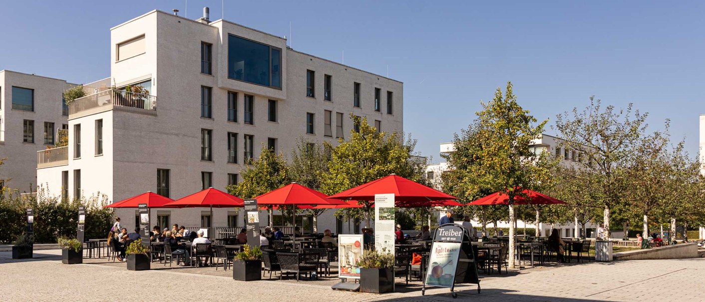 Moderne Wohngebäude in Stuttgart Killesberghöhe, mit roten Sonnenschirmen und Menschen auf einem Platz bei sonnigem Wetter., © Stuttgart-Marketing GmbH, Sarah Schmid Moderne Wohngebäude in Stuttgart Killesberghöhe, mit roten Sonnenschirmen und Menschen auf einem Platz bei sonnigem Wetter., © Stuttgart-Marketing GmbH, Sarah Schmid