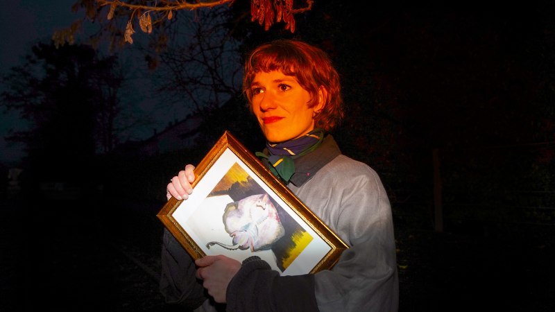 Eine Person steht in der Dunkelheit und h&auml;lt ein gerahmtes Bild. Sie ist von einem warmen Licht beleuchtet, w&auml;hrend der Hintergrund dunkel bleibt., &copy; Marina Buneta