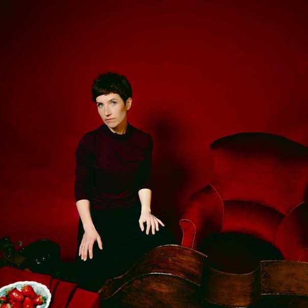 Frau sitzt in einem roten Raum neben einem roten Sessel. Ein Cello und eine Schale mit Erdbeeren sind zu sehen., © Judith Goldbach Frau sitzt in einem roten Raum neben einem roten Sessel. Ein Cello und eine Schale mit Erdbeeren sind zu sehen., © Judith Goldbach