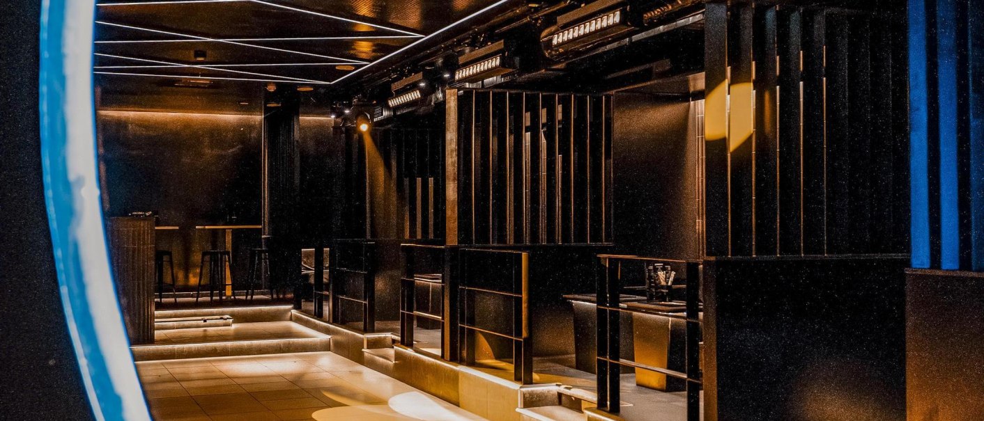 Moderner Nachtclub mit stilvoller Beleuchtung und geometrischen Linien. Dunkle, elegante Atmosphäre mit Sitzbereichen und Barhockern., © Wonders, Stuttgart