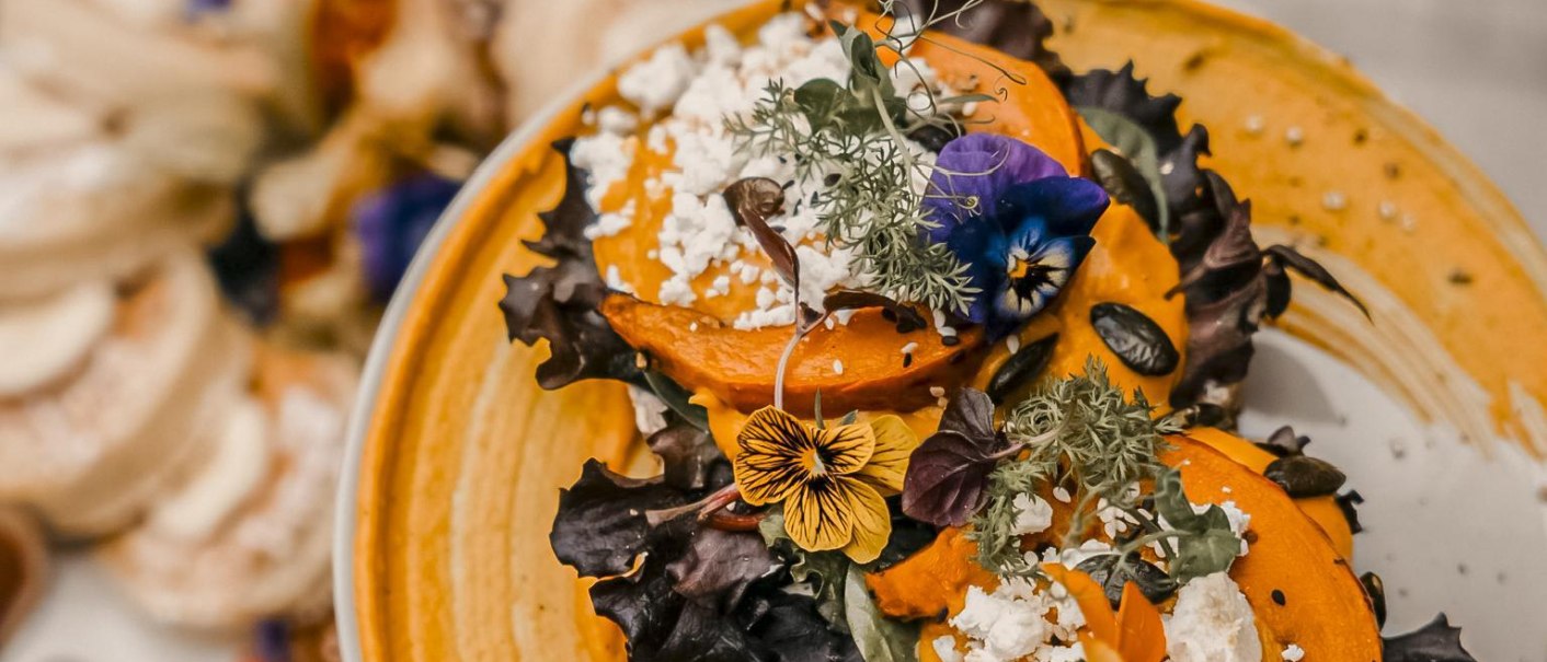 Ein kunstvoll angerichteter Teller mit Kürbis, essbaren Blüten und Salat auf einem orangefarbenen Püree., © Fritz Stuttgart