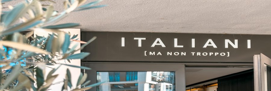 Entrance to a restaurant with the sign 'ITALIANI [MA NON TROPPO]'. Blurred plants can be seen in the foreground., &copy; SMG Stuttgart Marketing GmbH - Sarah Schmid