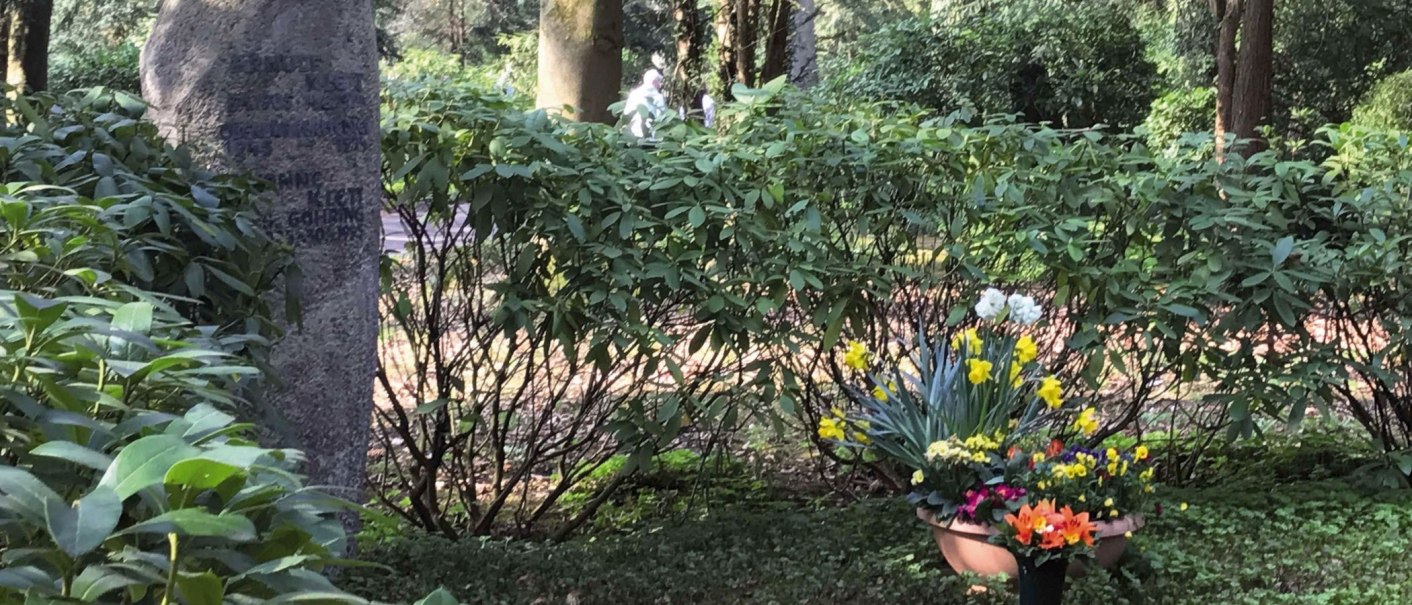 Ein Grabstein auf einem Waldfriedhof, umgeben von grünen Büschen. Vor dem Grabstein stehen bunte Blumen in Töpfen., © Stuttgart-Marketing GmbH
