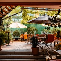Ein gemütlicher Innenhof eines Cafés mit Tischen, Stühlen und Sonnenschirmen, umgeben von grünen Pflanzen und Bäumen., © SMG_Sarah Schmid Ein gemütlicher Innenhof eines Cafés mit Tischen, Stühlen und Sonnenschirmen, umgeben von grünen Pflanzen und Bäumen., © SMG_Sarah Schmid