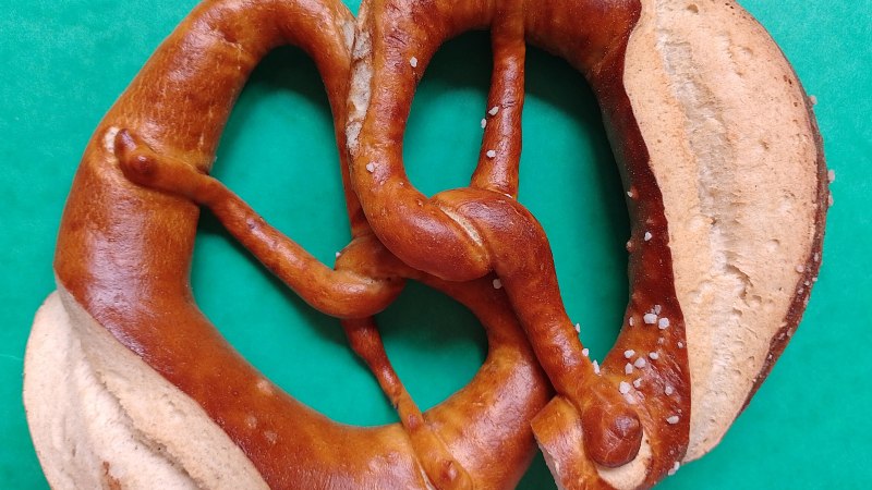 Eine Brezel liegt auf einem grünen Hintergrund. Die Brezel ist goldbraun mit grobem Salz bestreut., © Svenja Rehse