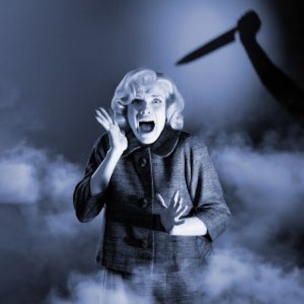 Eine Frau schreit erschrocken, während der Schatten einer Person mit Messer im Hintergrund sichtbar ist. Die Szene ist in blauem Licht gehalten., © Altes Schauspielhaus und Komödie im Marquardt e.V.