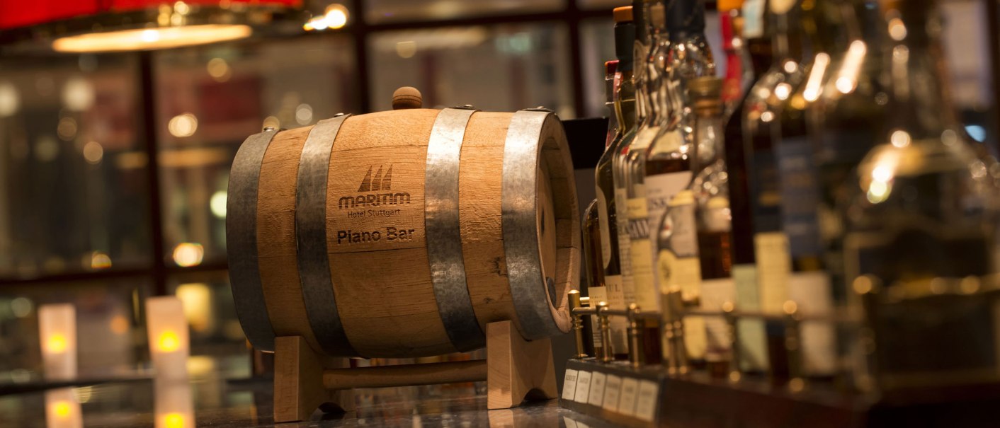 A wooden barrel with the inscription 'Maritim Hotel Stuttgart Piano Bar' stands on a bar, surrounded by various bottles and candlelight., &copy; Maritim Hotels