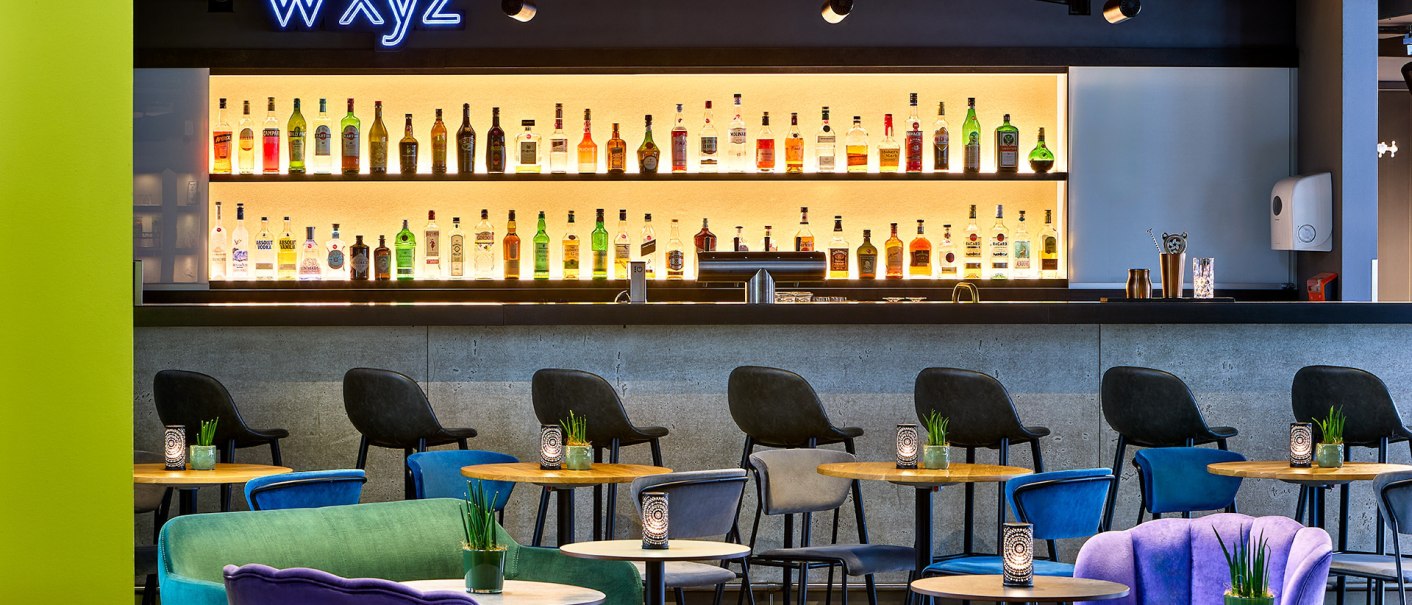 Modern bar with colorful armchairs and illuminated bottle rack. The lettering "WXYZ" lights up above the bar., &copy; Aloft Stuttgart