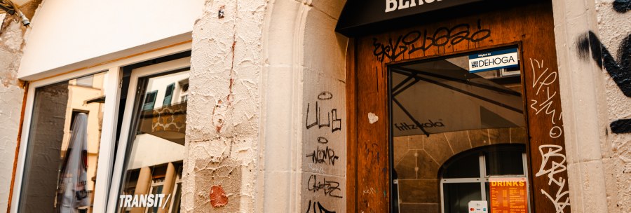 Entrance with the inscription 'Transit Bergamo' above the door, surrounded by graffiti. A window shows reflections of the surroundings., © Sarah Schmid Entrance with the inscription 'Transit Bergamo' above the door, surrounded by graffiti. A window shows reflections of the surroundings., © Sarah Schmid