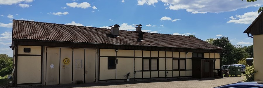Half-timbered building with a tiled roof and chimneys, surrounded by trees and cars. The sky is blue with a few clouds., © Weinbau Glock und Sohn GbR Half-timbered building with a tiled roof and chimneys, surrounded by trees and cars. The sky is blue with a few clouds., © Weinbau Glock und Sohn GbR