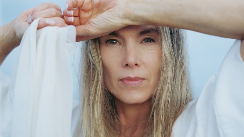 Eine Frau mit langen blonden Haaren h&auml;lt einen wei&szlig;en Stoff und blickt direkt in die Kamera. Der Hintergrund ist blau und wolkig., &copy; Theaterhaus Stuttgart e.V.