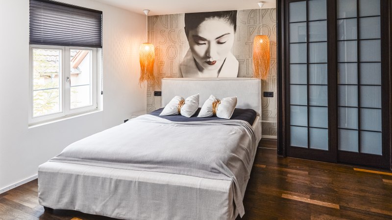 Modern hotel room with large bed, mural of a woman, two hanging lamps and wooden floor., © Zauberlehrling