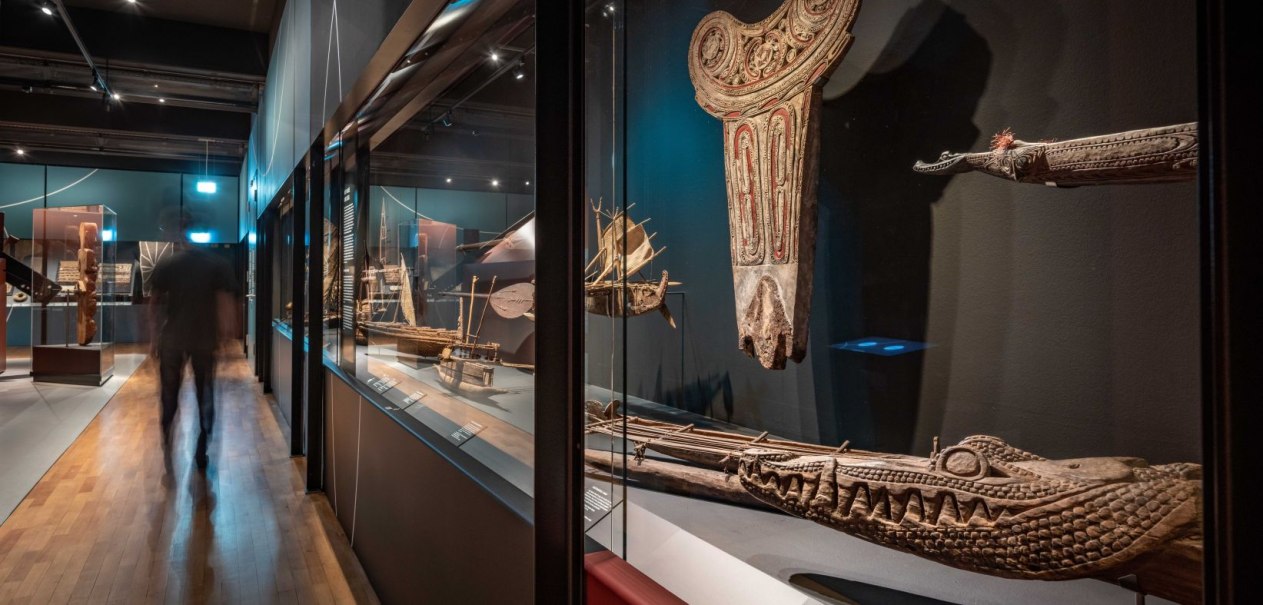 Ein Museumsraum mit ozeanischen Kunstwerken und Modellen von Booten in Glasvitrinen. Eine Person geht durch den Raum., &copy; Linden-Museum Stuttgart