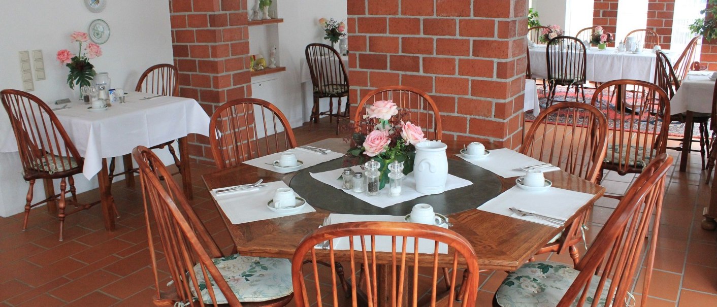 A cozy dining room with wooden tables and chairs, brick walls, and decorative flower arrangements on the tables., &copy; Hotel Spahr