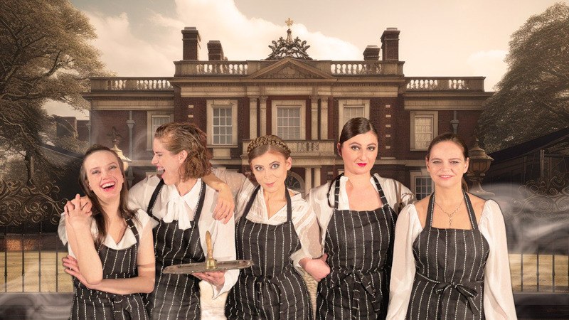 Fünf Frauen in gestreiften Schürzen stehen lächelnd vor einem großen Herrenhaus. Der Himmel ist bewölkt, und es gibt leichten Nebel., © tri-bühne e.V. Fünf Frauen in gestreiften Schürzen stehen lächelnd vor einem großen Herrenhaus. Der Himmel ist bewölkt, und es gibt leichten Nebel., © tri-bühne e.V.